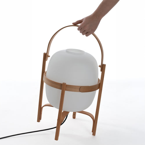A hand carrying the Cesta lamp by its curved wooden handle