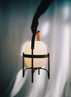 A hand carrying the Cestita Batería portable lamp by its handle