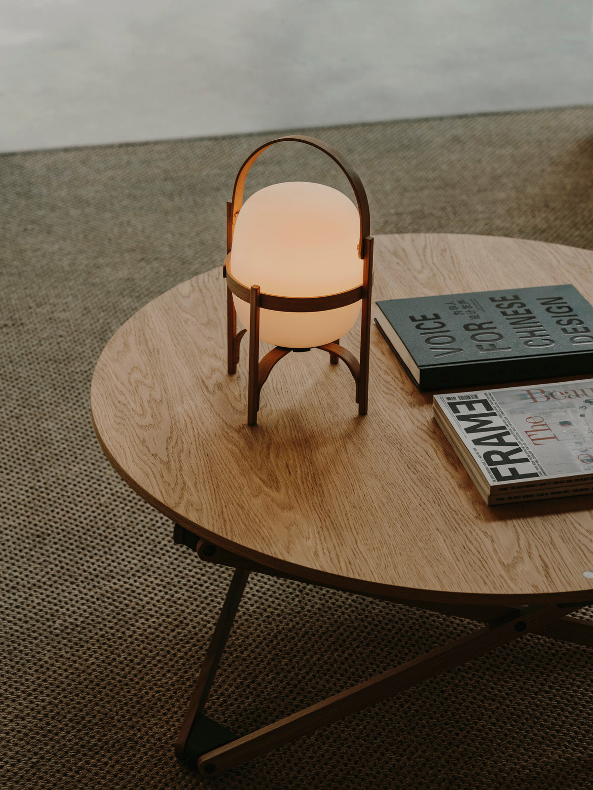 Cestita Batería portable lamp on a round wooden coffee table beside books