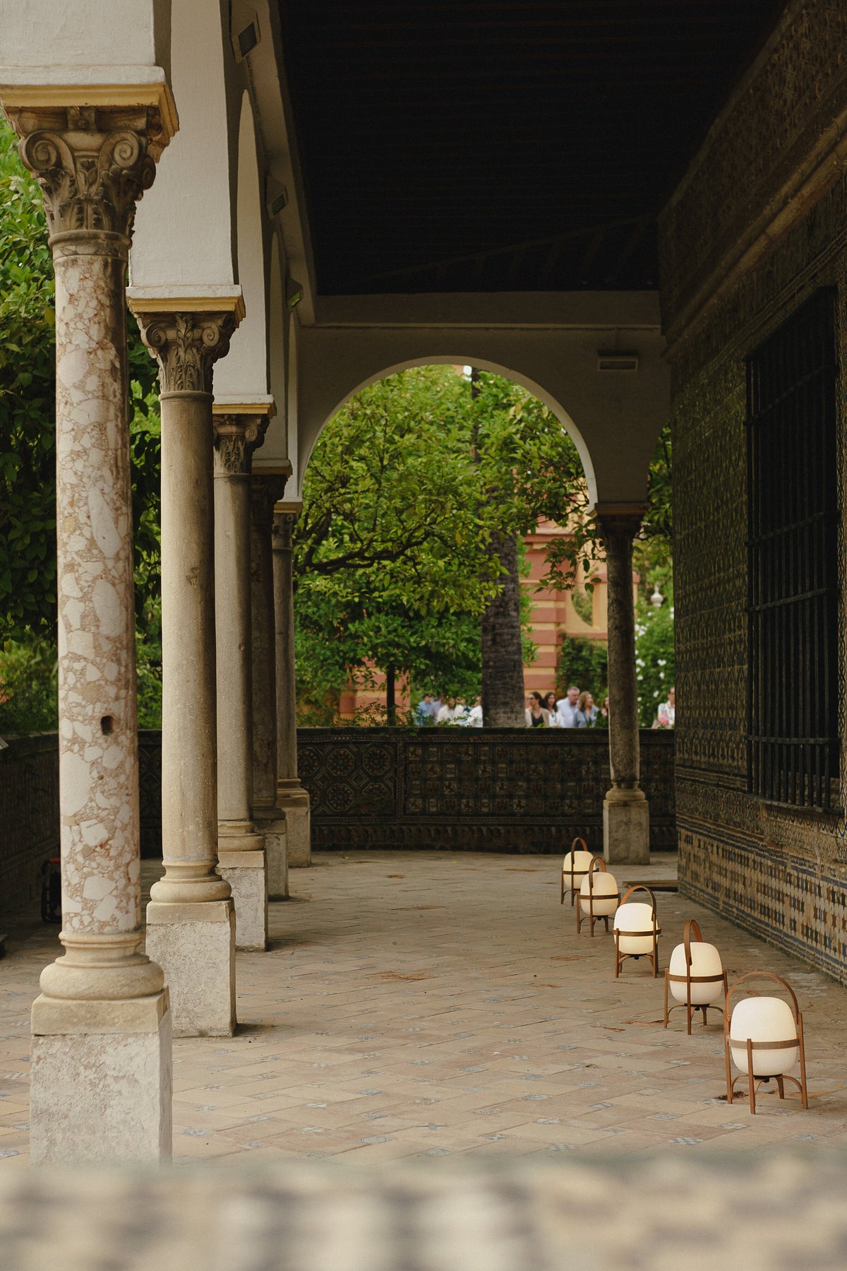 A row of Cestita Batería portable lamps along a colonnaded walkway at night
