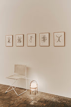 Cestita Batería portable lamp on the floor beside a chair, below framed drawings