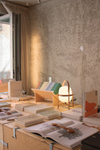 Cestita lamp switched on at a desk covered with books and paper