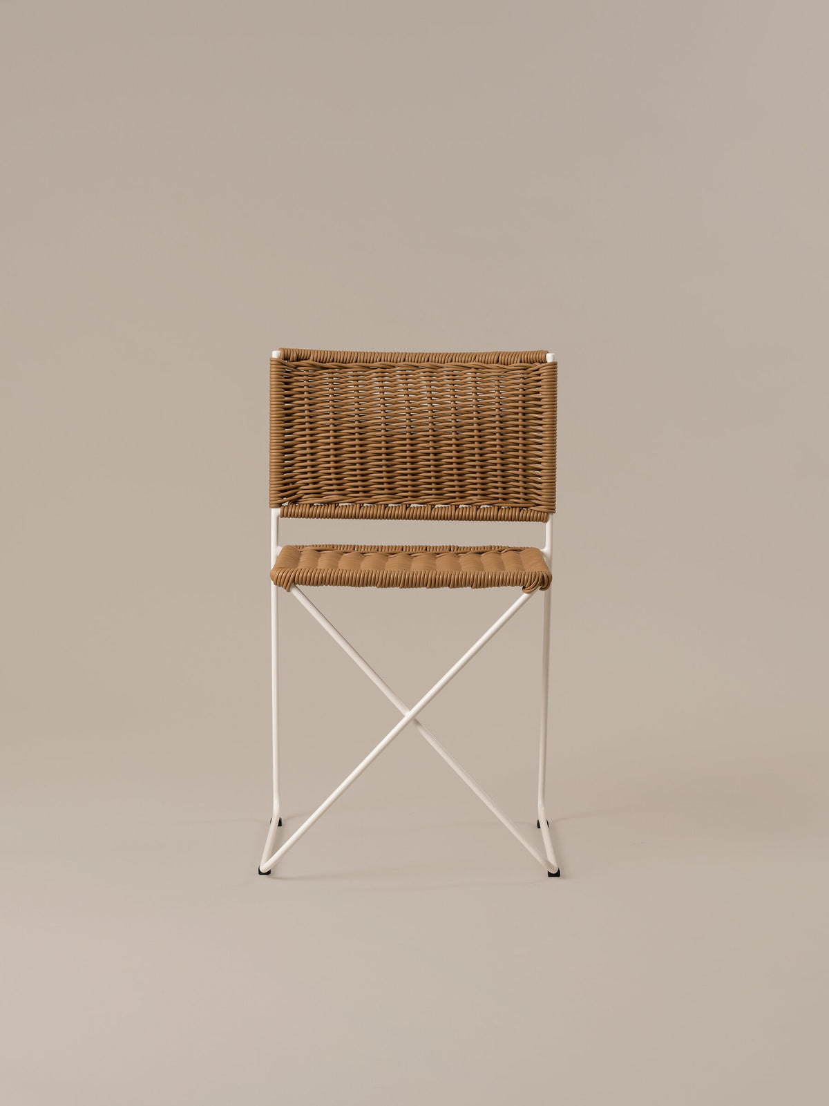 Front view of the Ramón chair in natural rattan, showing the crossed bar beneath the seat