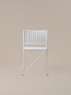 Front view of the Ramón chair in white rattan, showing the crossed bar beneath the seat