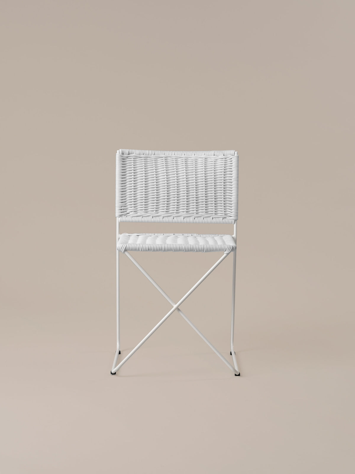 Front view of the Ramón chair in white rattan, showing the crossed bar beneath the seat