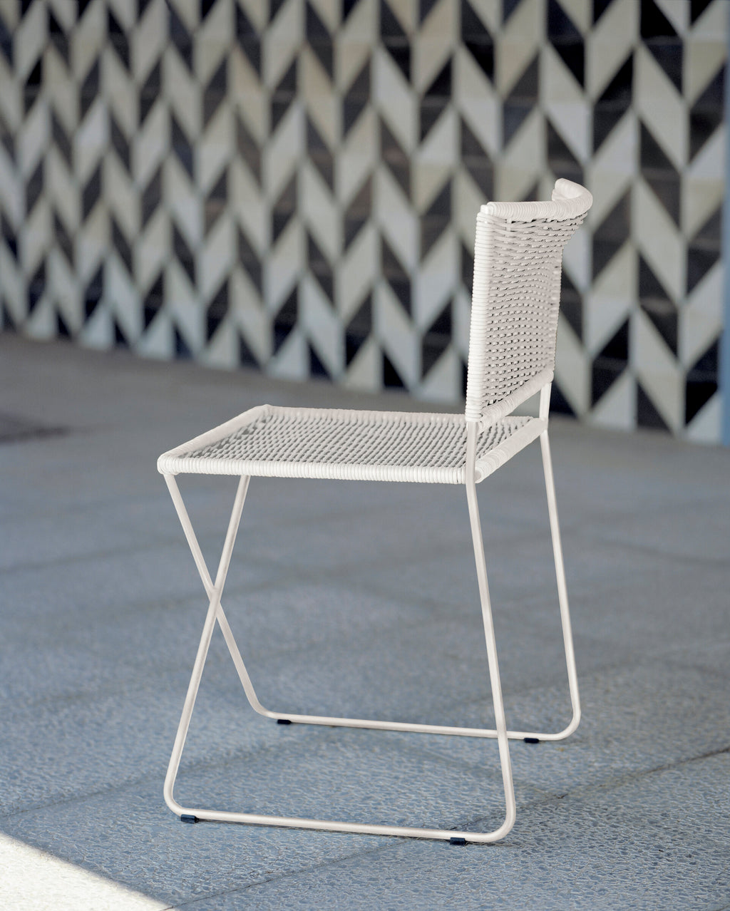 Ramón chair in white rattan on a terrace in front of a patterned tiled wall