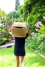 A person carrying a Ramón chair on their head through a garden