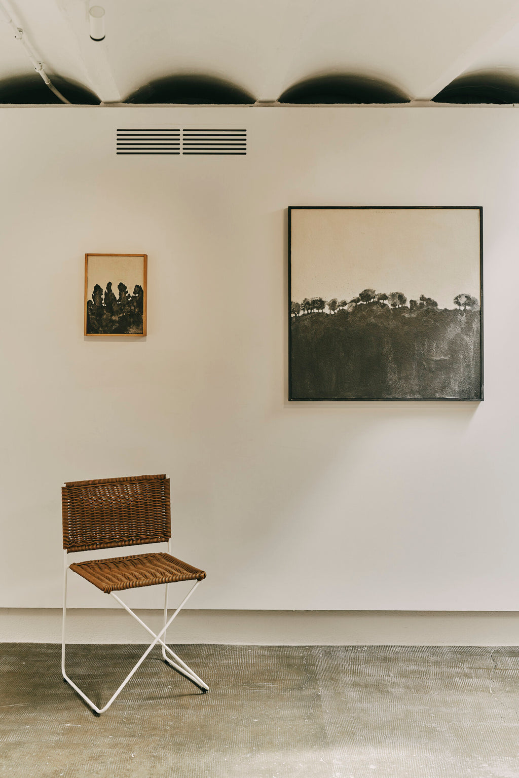 Ramón chair in natural rattan in a gallery, beneath framed paintings