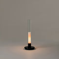 Sylvestrina portable lamp by Santa & Cole with a black base and clear glass tube, switched on