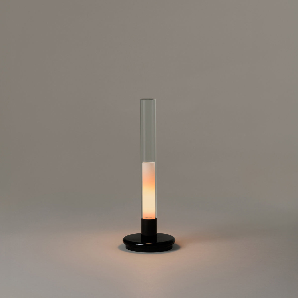 Sylvestrina portable lamp by Santa & Cole with a black base and clear glass tube, switched on