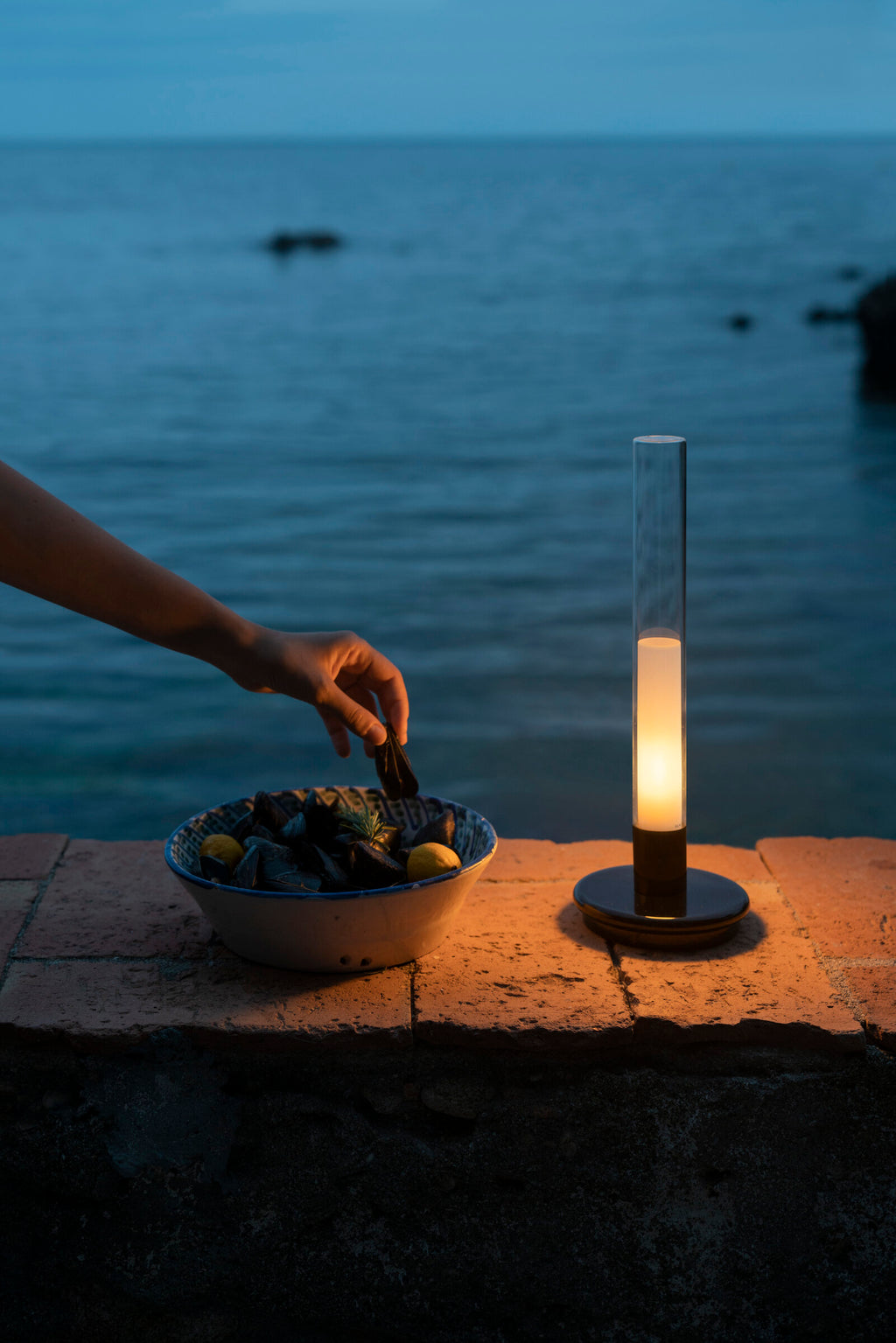 Sylvestrina portable lamp on a stone ledge by the sea at dusk