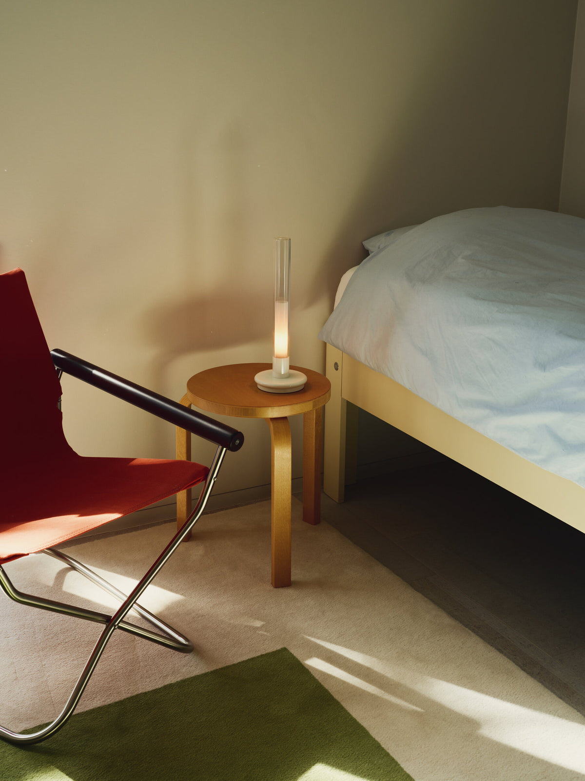 Sylvestrina portable lamp on a bedside stool beside a red folding chair