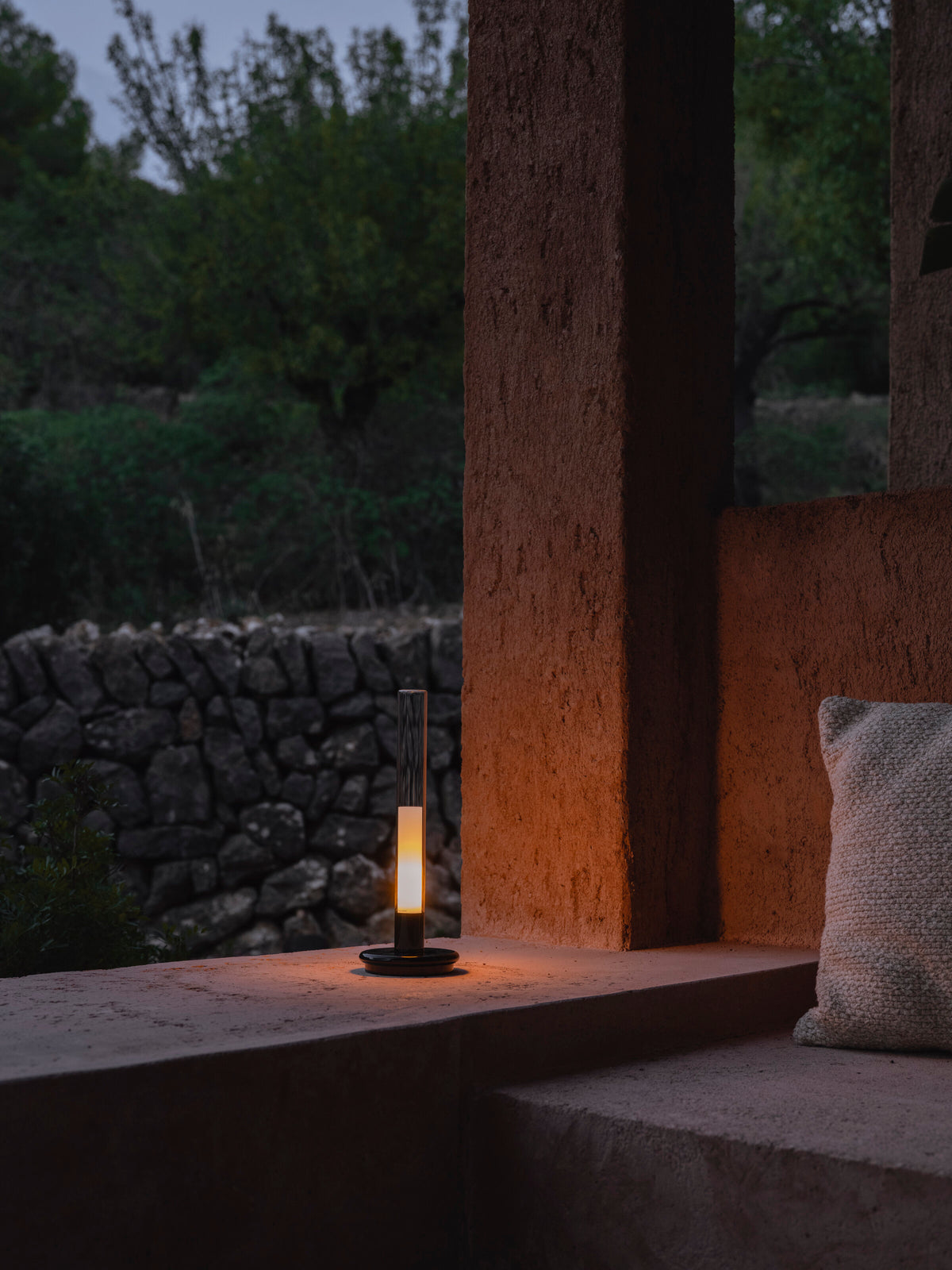 Sylvestrina portable lamp on a terrace at dusk beside a dry stone wall