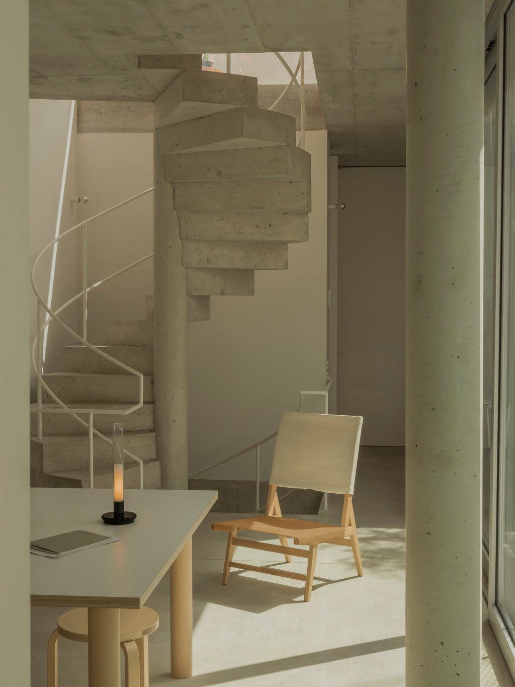 Sylvestrina portable lamp on a table beside a lounge chair and spiral staircase
